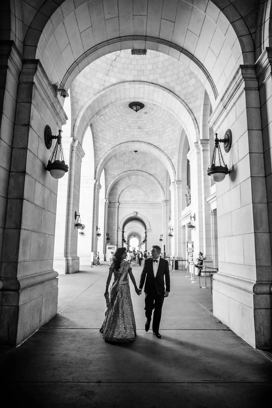 A couple hold hands and look at one another under an archway outside Union Station. The moment is captured in black and white.