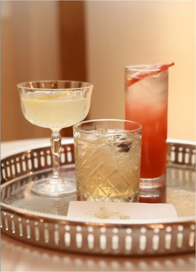 Three cocktails in clear glasses on a round silver tray.