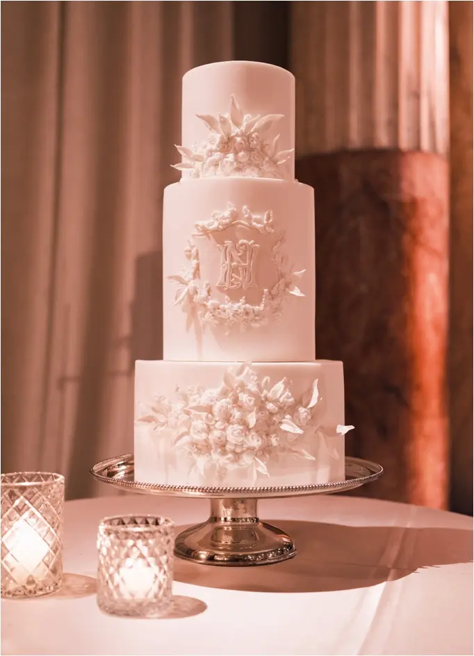 An intricately designed three-tier white wedding cake featuring white florals and the couple's personalized wedding monogram.